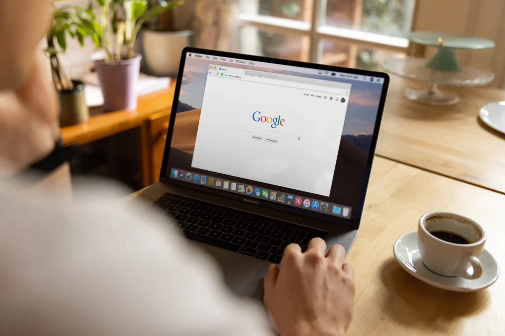 Person at a cafe table searching Google on a laptop, the starting point for checking which links show up for a name or brand