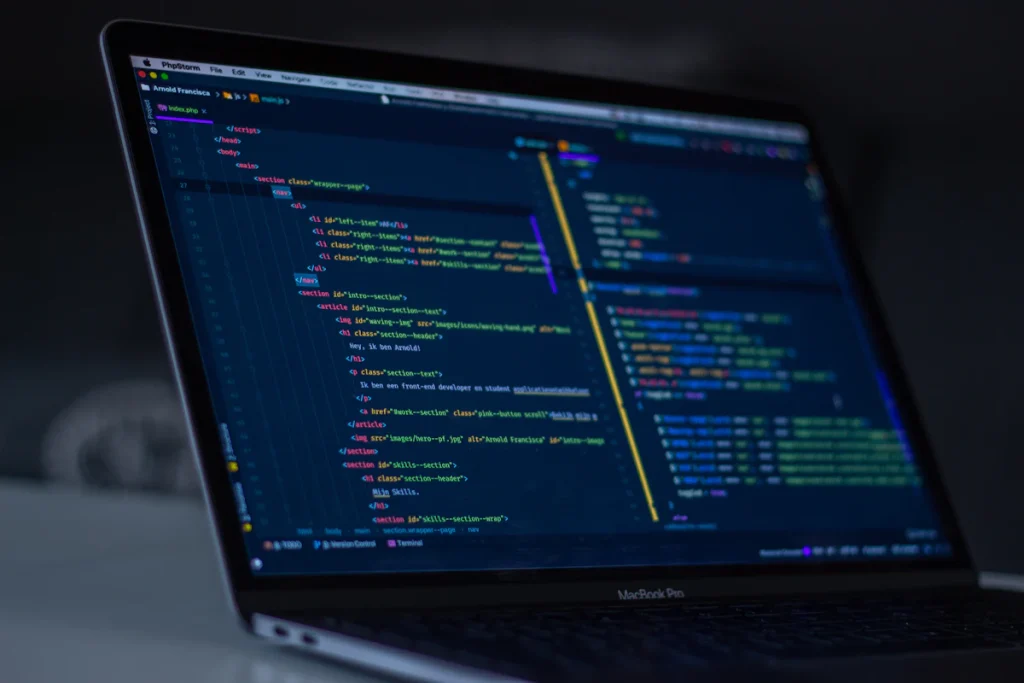 MacBook Pro on a desk showing colour-highlighted programming code in a dark editor