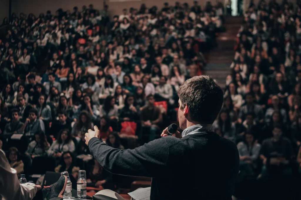 Speaker on stage presenting ideas to a seated conference audience, a classic way to build thought leadership