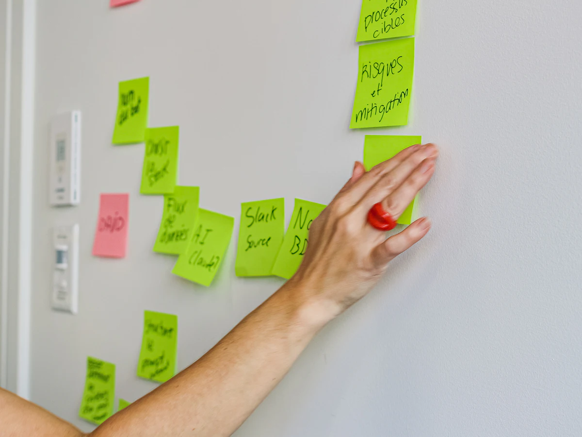 Hand placing a sticky note on a wall to shortlist AI-generated ideas for review