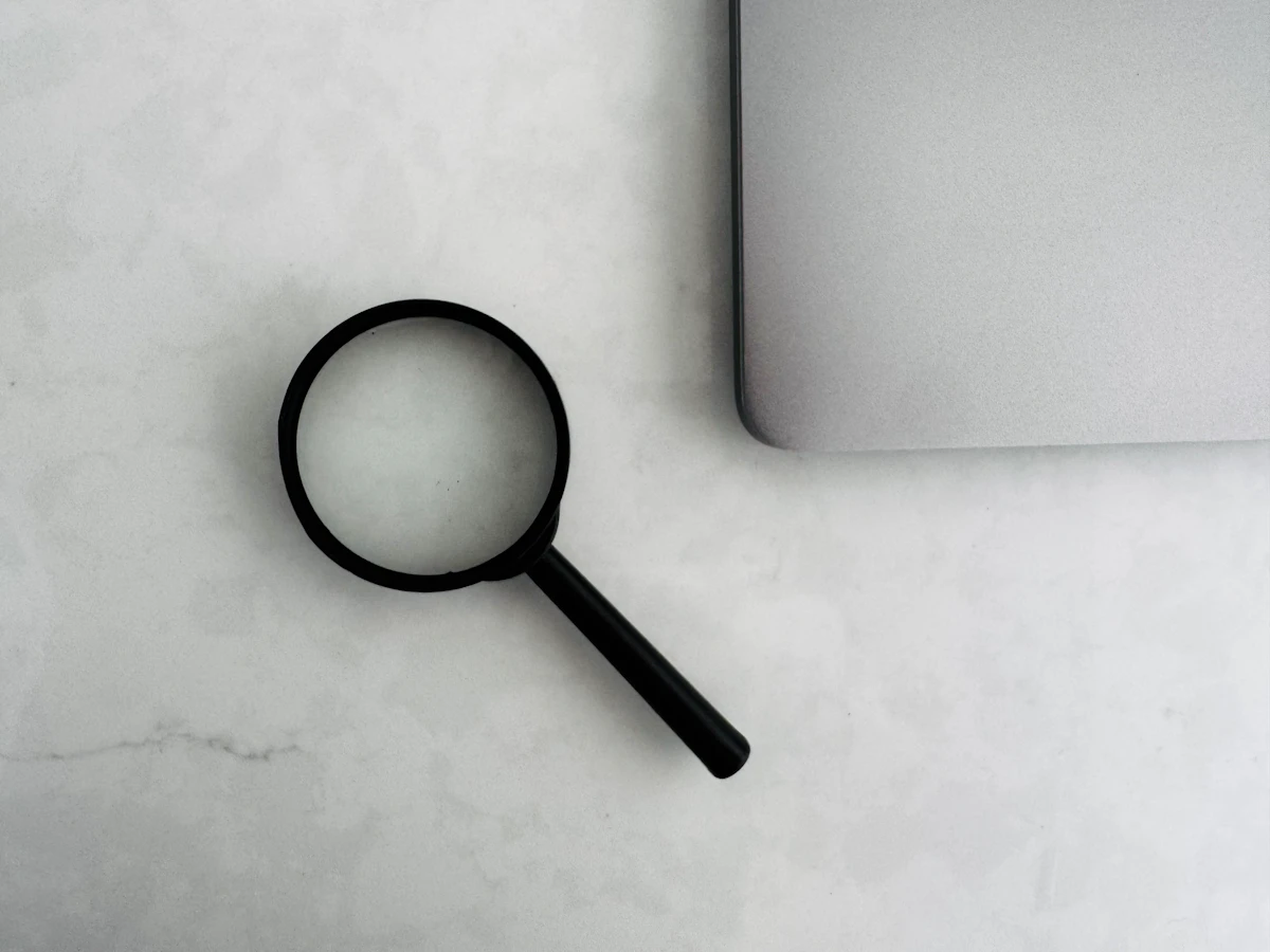 Magnifying glass resting beside the corner of a laptop on a marble desk, a reminder to inspect search results closely