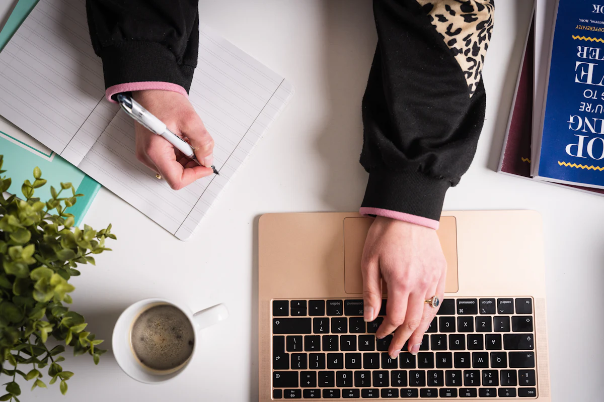 Overhead view of a laptop, notebook and coffee on a desk while someone drafts and plans articles